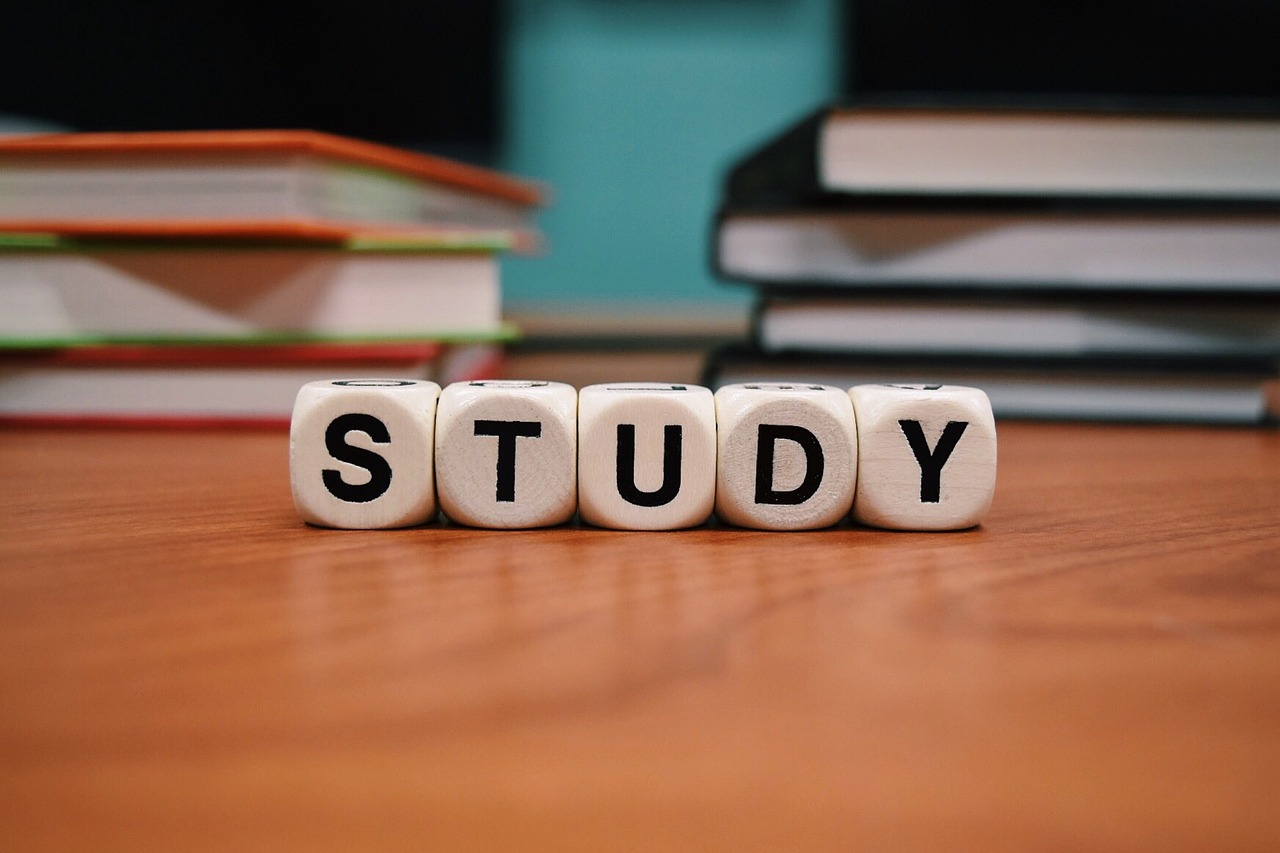 Image is of books in the background, with scrabble blocks spelling the word study in the foreground.